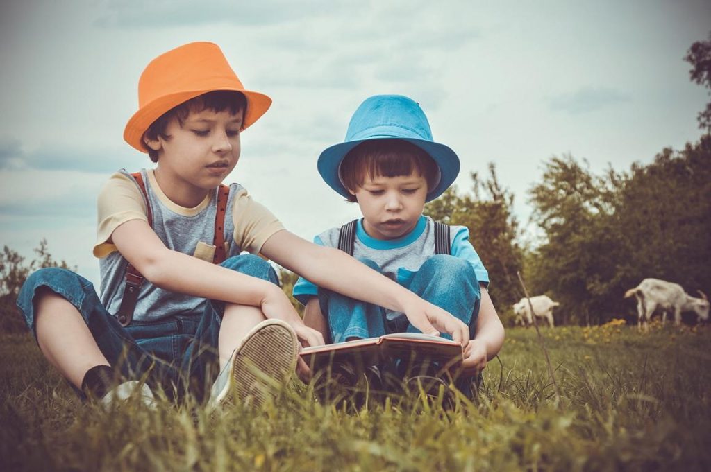 Foto: zwei Jungs sitzen auf einer Ziegenwiese und schauen interessiert in ein Buch